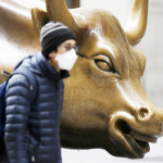 株価上昇を象徴する米ウォール街のチャージング・ブル像の前を新型コロナ感染拡大後にマスク姿で歩く人（ＵＰＩ）