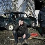２４日、爆撃を受けたウクライナ東部ハリコフ近郊で、損壊した建物の前で座り込む男性（ＡＦＰ時事）