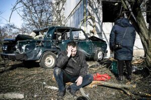 ２４日、爆撃を受けたウクライナ東部ハリコフ近郊で、損壊した建物の前で座り込む男性（ＡＦＰ時事）